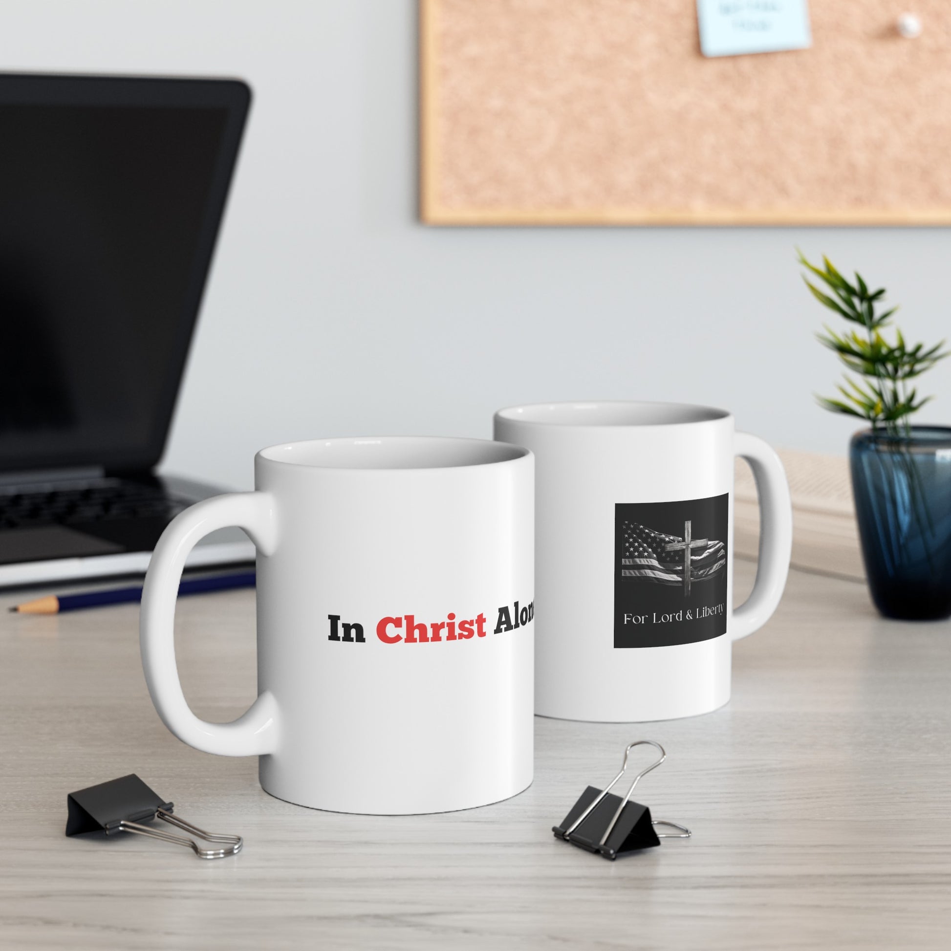 a white mug that says In Christ Alone and another mug with the for lord and liberty logo that is sitting on a desk