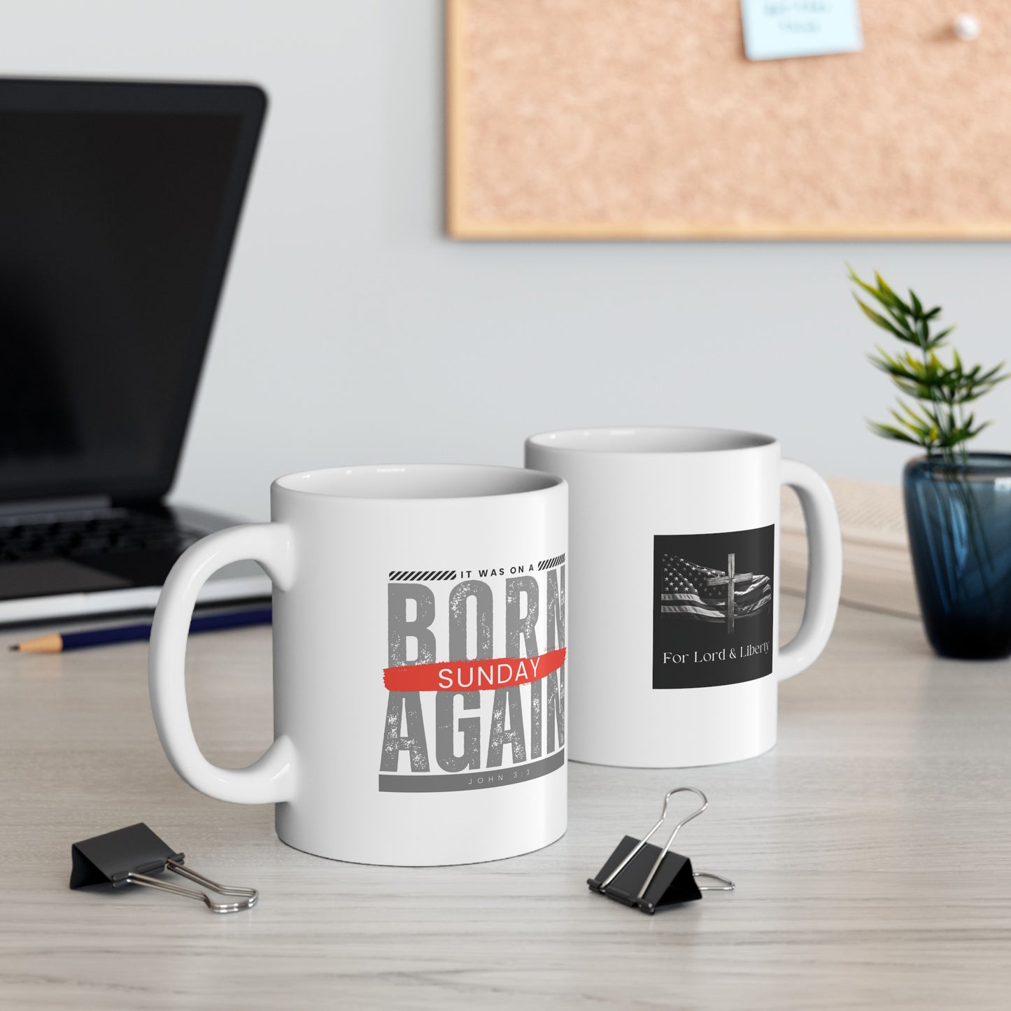 a white mug with the words Born Again it was on a Sunday John 3:3 and the other mug has the for lord and liberty logo that is sitting on a desk