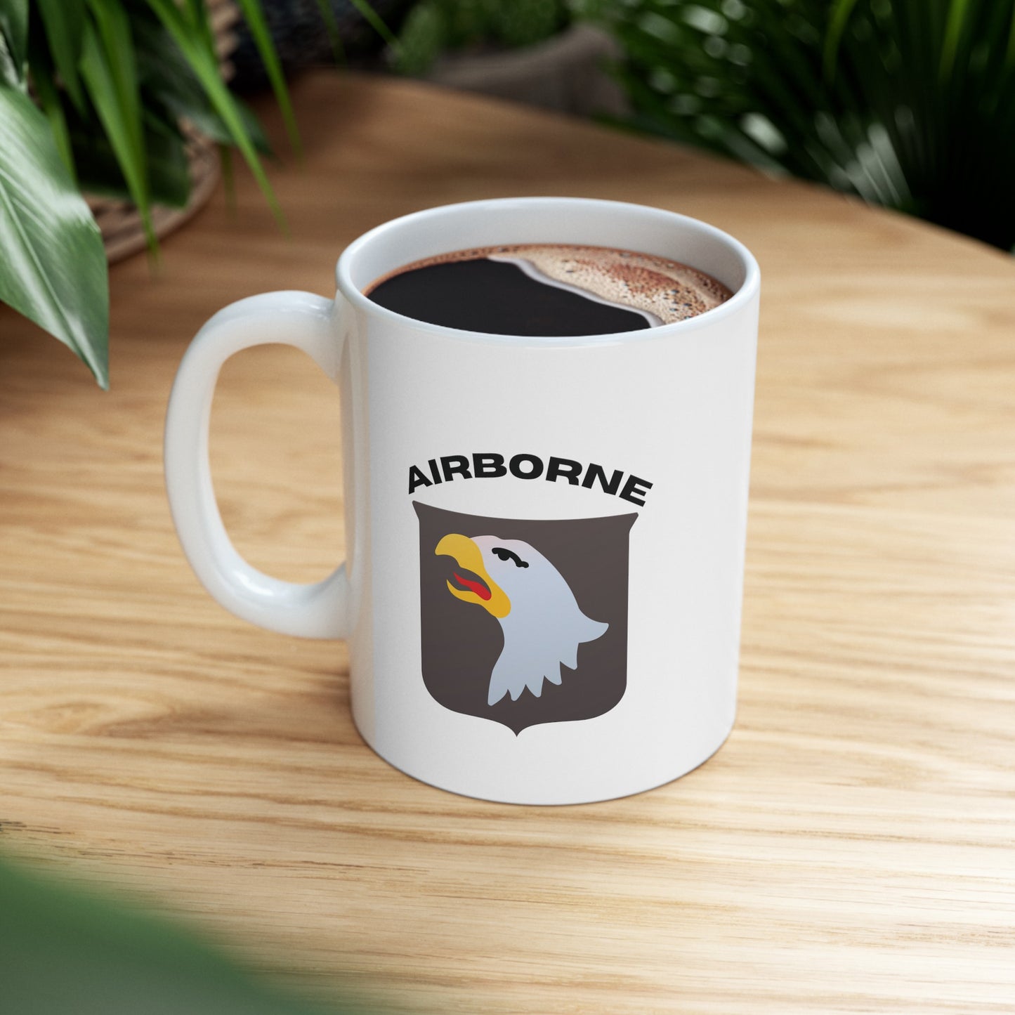 a white mug with the 101st Airborne logo with the words Airborne in black sitting on a table