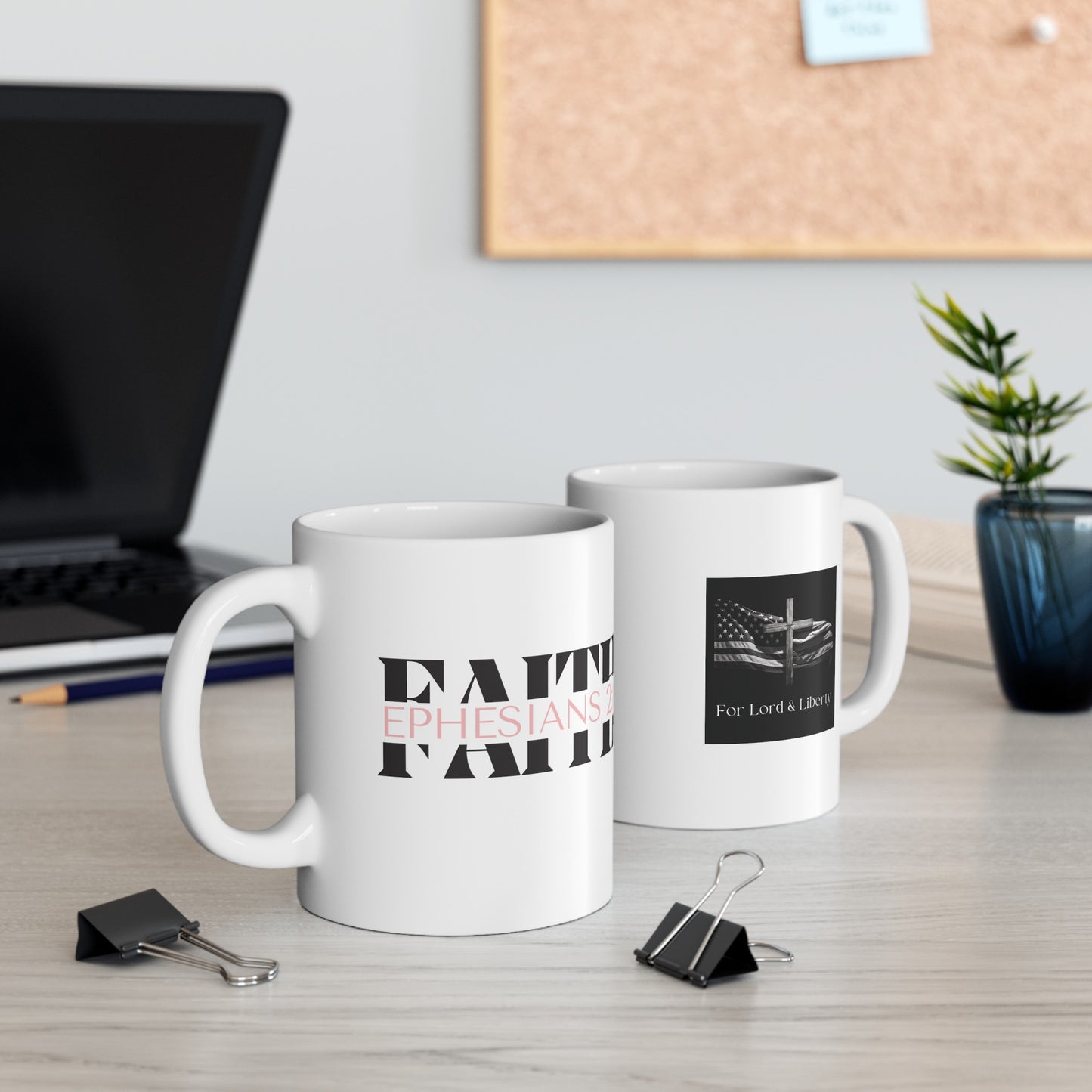 a white mug with the words FAITH Ephesians 2:8 and another mug with the for lord and liberty logo that is sitting on a desk