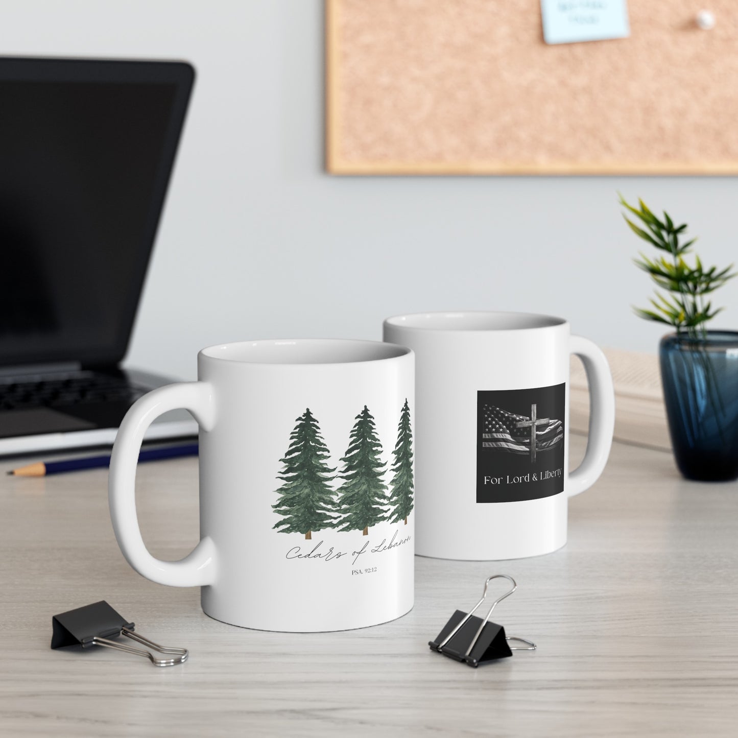 a white mug with three cedar trees with the words cedars of lebanon Psa. 92:12 and another mug with the for lord and liberty logo that is sitting on a desk