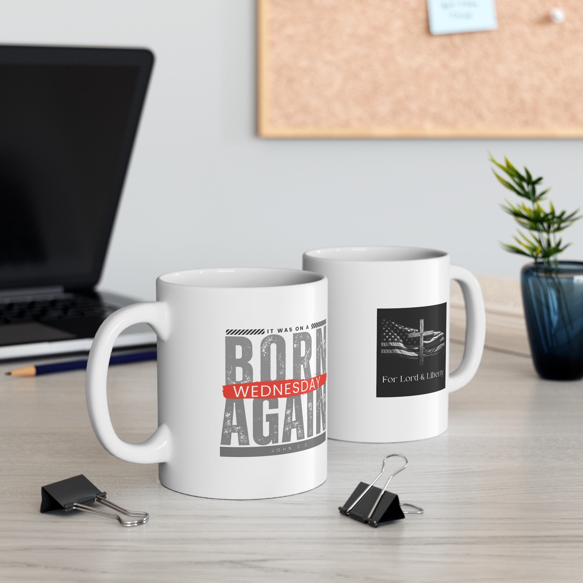 a white mug with the words Born Again it was on a Wednesday John 3:3 and another mug with the for lord and liberty logo sitting on a desk