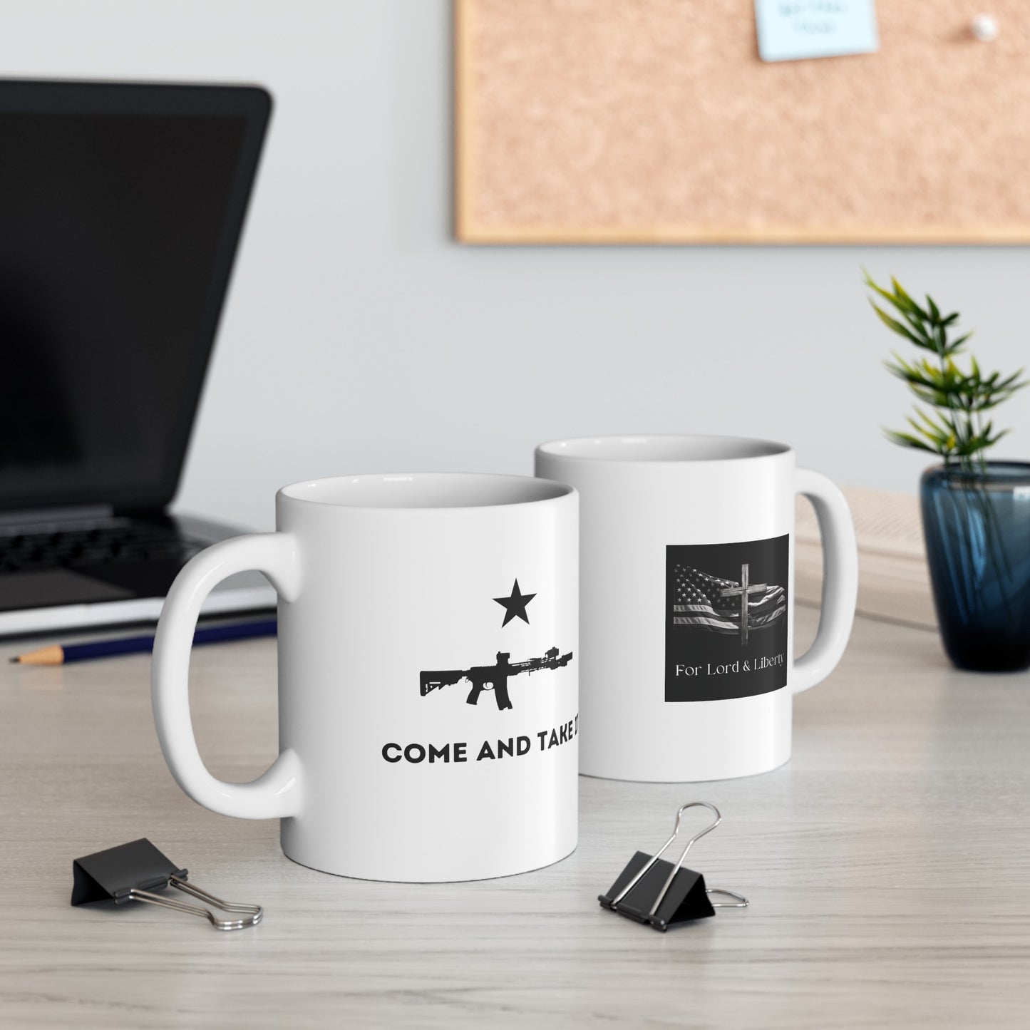 A white mug with the words come and take it with an m-4 rifle and another with the for lord and liberty logo sitting on a desk