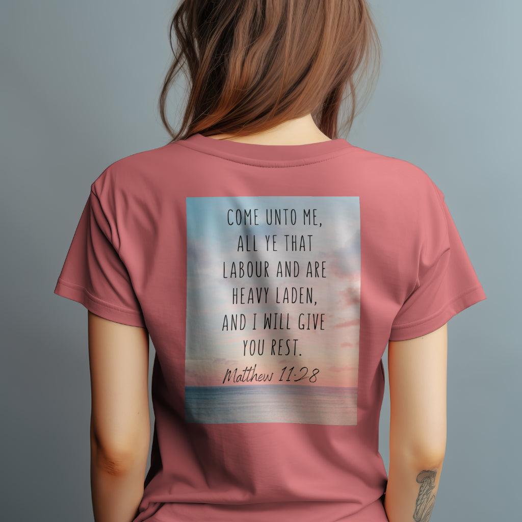 a woman wearing a coral silk color t-shirt with tranquil imagery with the Scripture Matthew 11:28: "Come unto me, all ye that labour and are heavy laden, and I will give you rest."