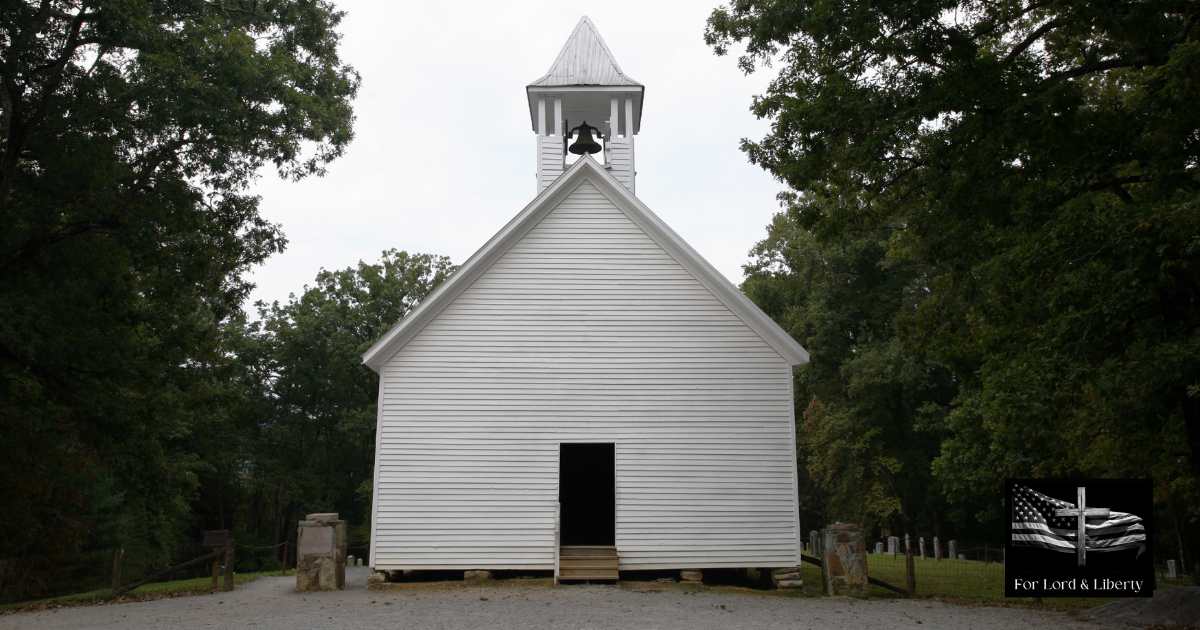 White wooden country church with a bell tower, surrounded by trees
