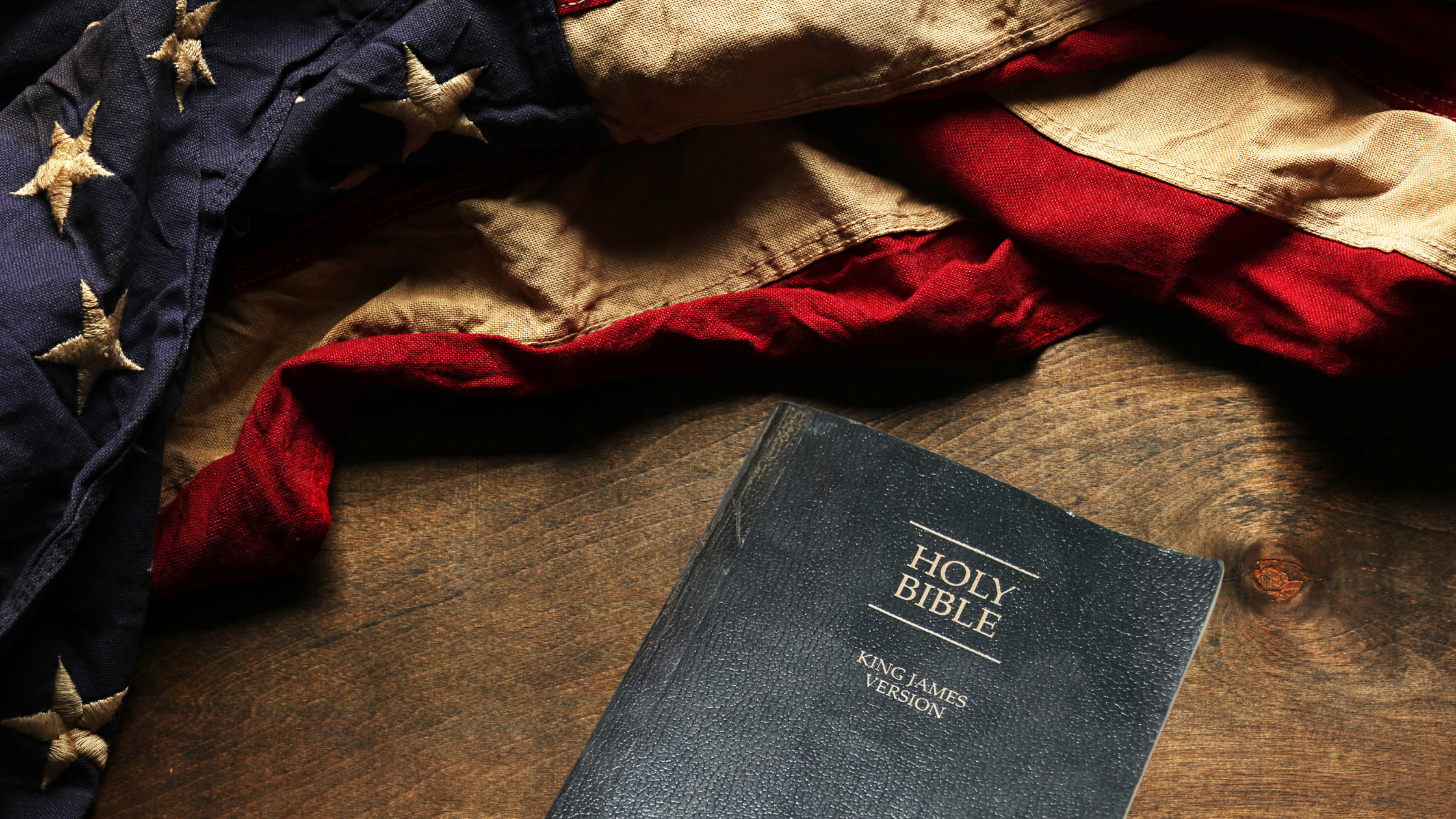 A distressed American flag on a table with a King James version Holy Bible